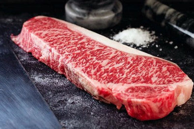 Raw steak on a dark surface with salt and pepper shakers in the background
